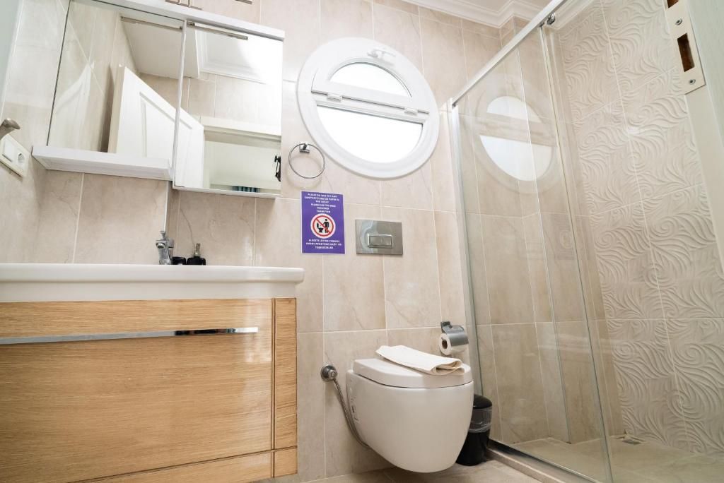 A bathroom with a toilet, a sink, a mirror, and a shower enclosure.
