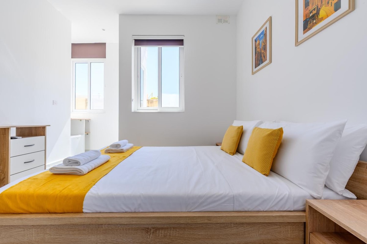 A hotel room with a bed, a wooden nightstand, a desk, and a chair.