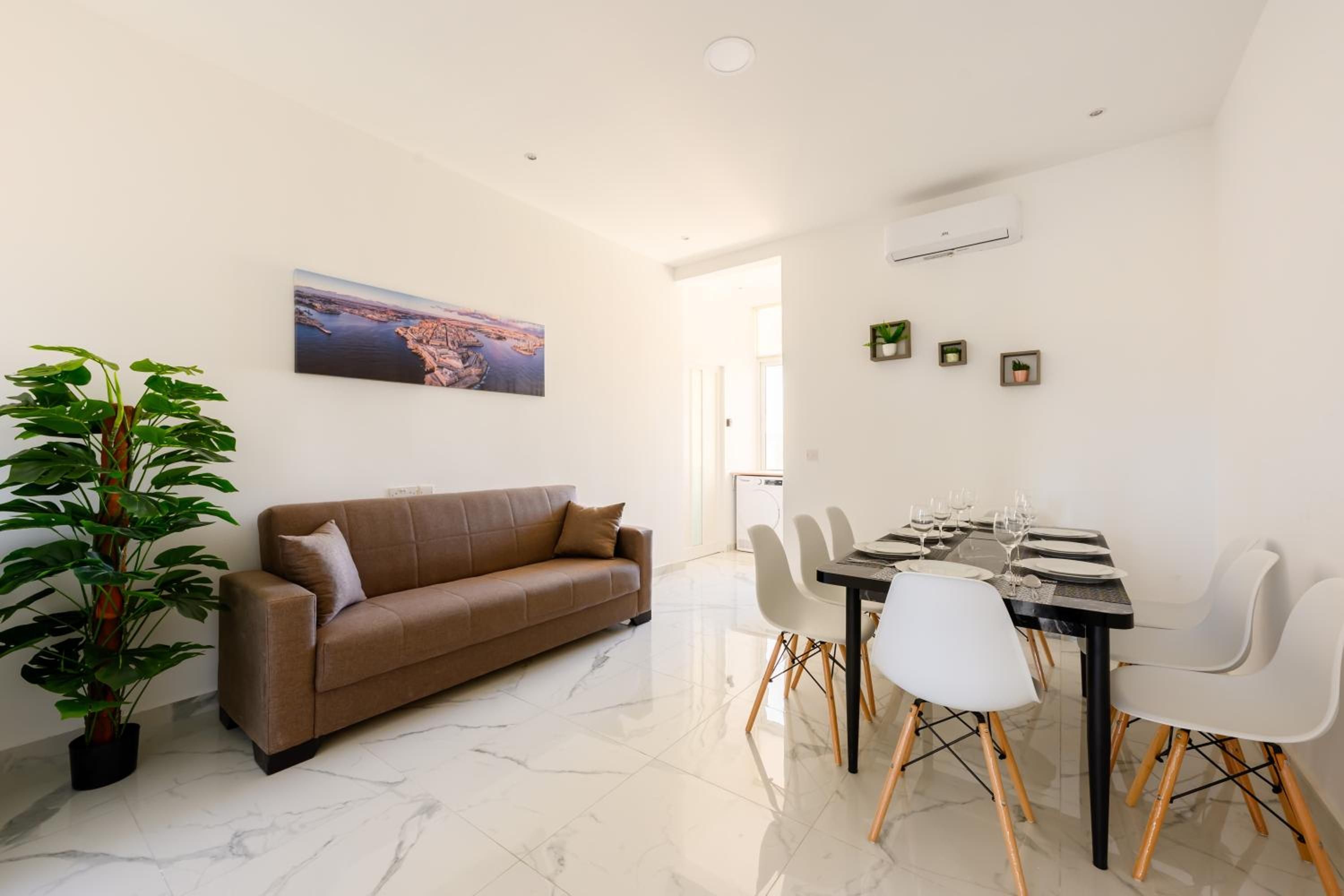 Una sala de estar moderna con un sofá marrón, una mesa de comedor lista para seis personas y una gran planta en maceta.