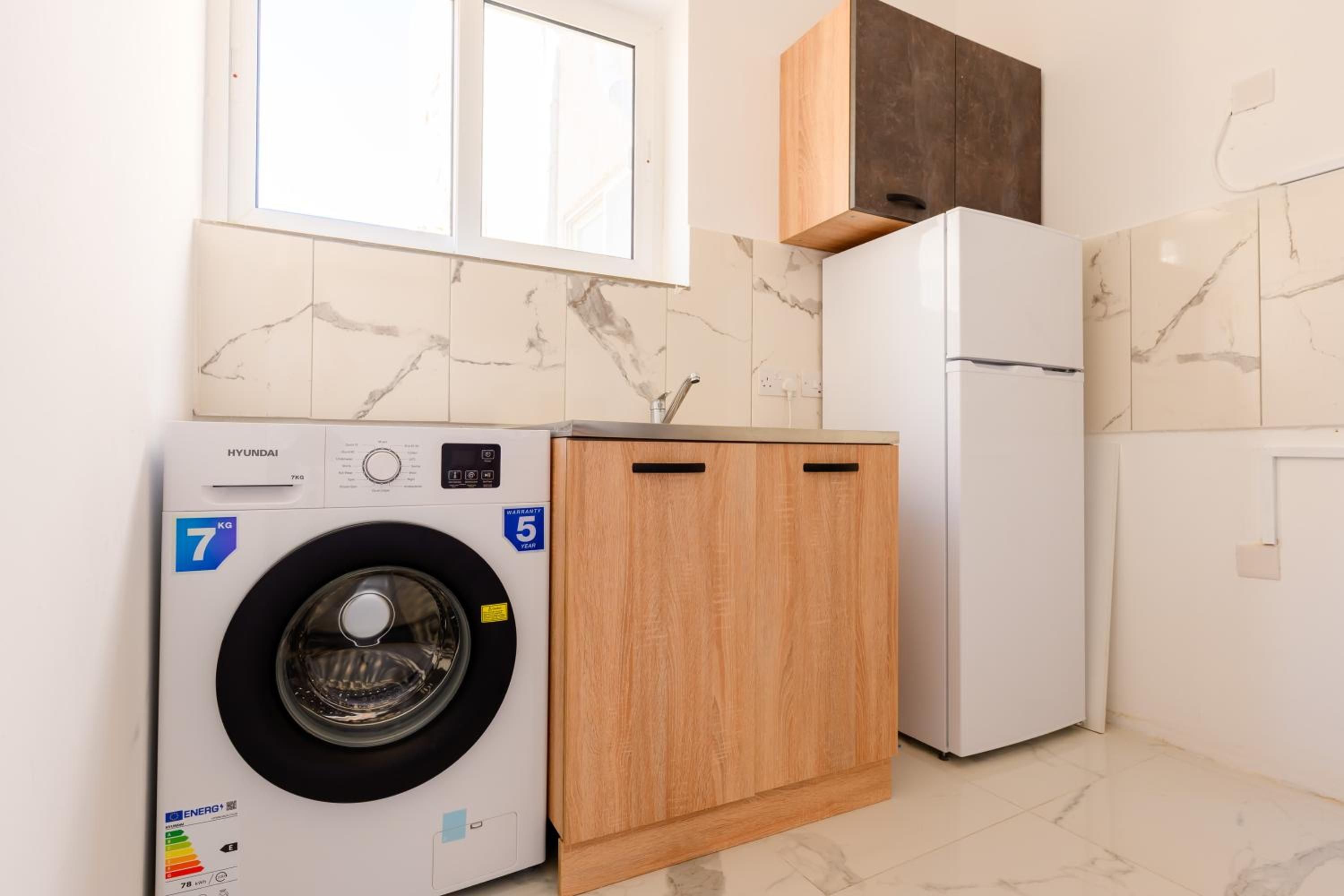 Une cuisine de taille réduite équipée d’un lave-linge, d’un réfrigérateur et de meubles de rangement en bois.