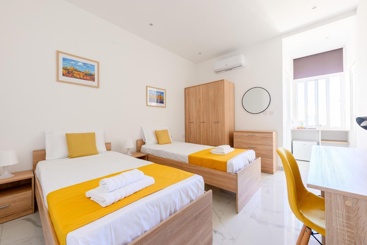 A hotel room with two beds, a wardrobe, a desk, and a chair.