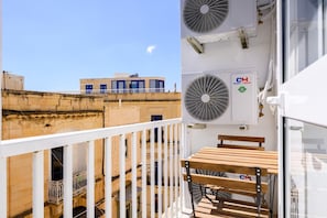 A balcony with a table and chairs, overlooking a building with multiple windows and a rooftop. - RODOLFU F8 (Tas-Sliema)