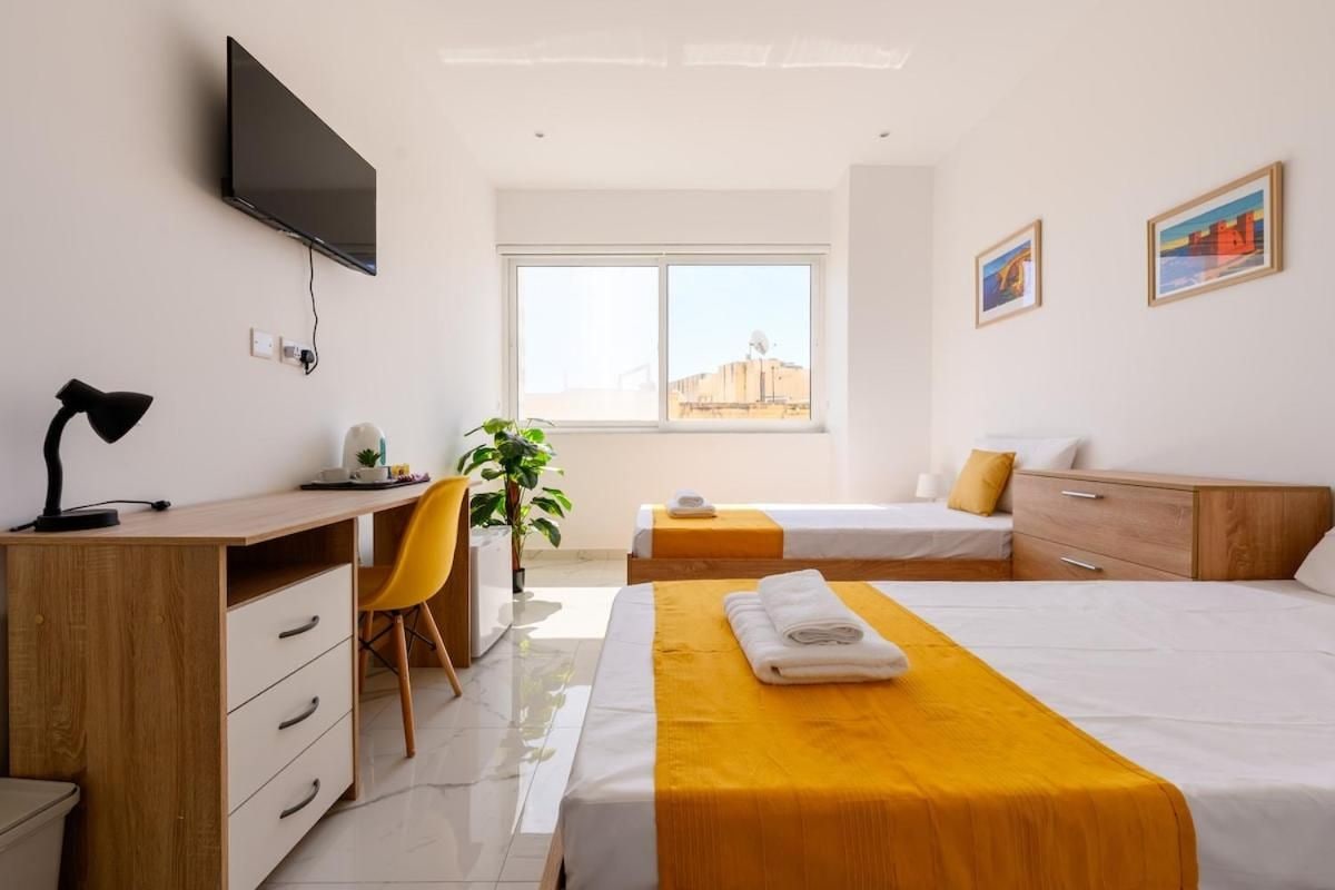 A hotel room with a bed, desk, chair, TV, and a window with a city view.