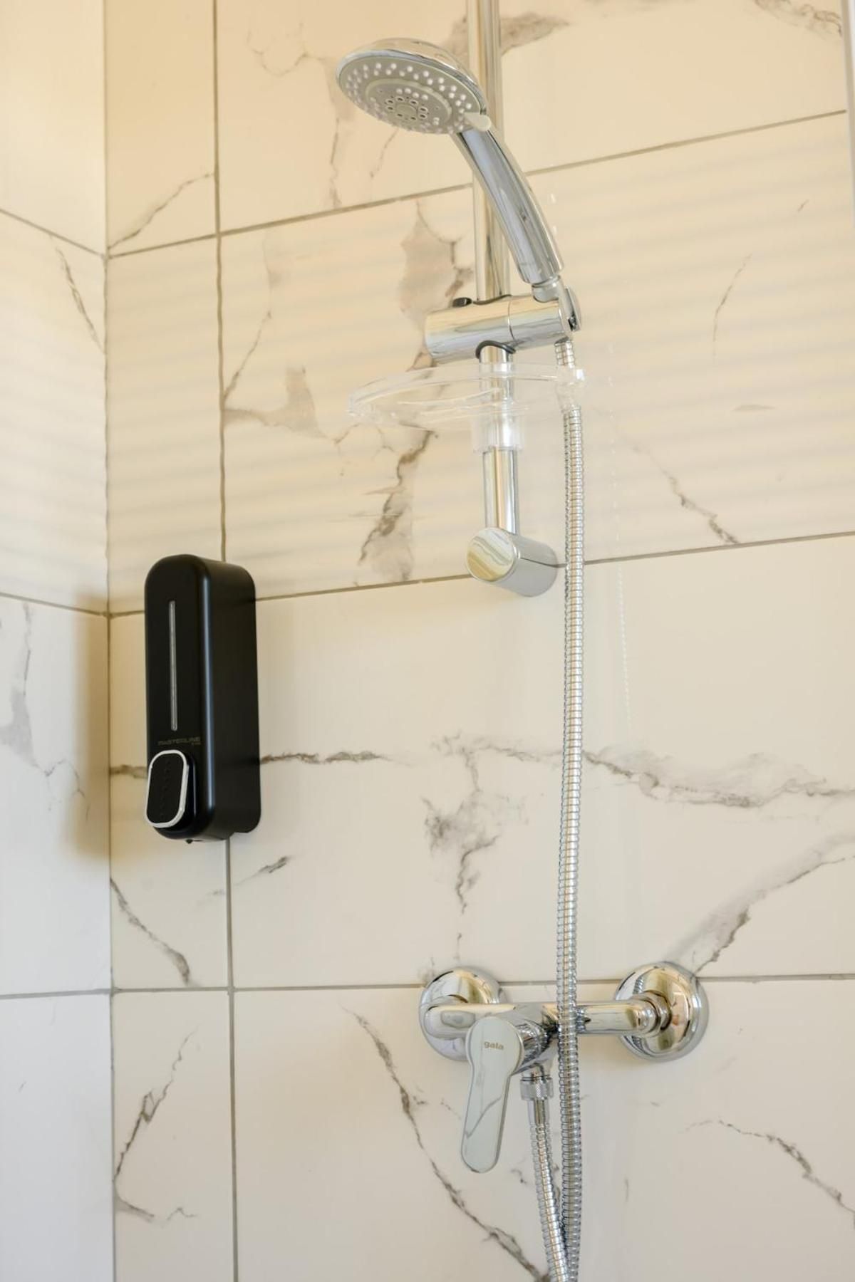 A bathroom with a shower, a handheld showerhead, and a soap dispenser.