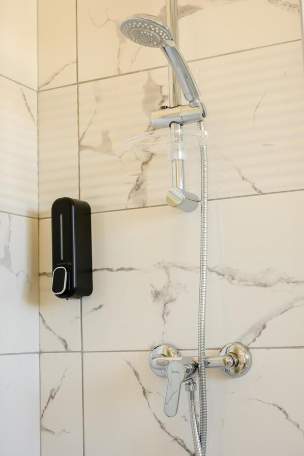 A bathroom with a shower, a handheld showerhead, and a soap dispenser.