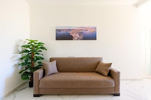 A living room with a sofa, a potted plant, and a painting on the wall.