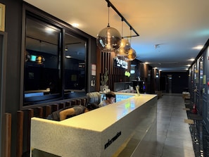 Um hall de hotel com balcão de recepção, área de estar e uma janela ampla.