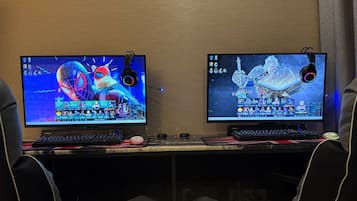 Zwei Computermonitore auf einem Schreibtisch mit Gaming-Zubehör, was auf einen Gaming-Einrichtung hindeutet.
