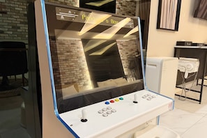 A gaming machine with a screen, joystick, and buttons, located in a room with a brick wall and a white tiled floor. - SUWON 3S HOTEL STAR (HOMAESIL) (Suwon)