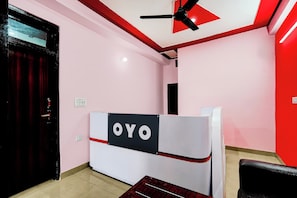 A reception area with a red and white color scheme, a ceiling fan, and a reception desk with 'OYO' branding. - Hotel O Moonville Pusta (Noida)