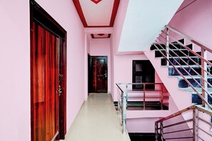 A corridor with a wooden door, a staircase with metal railings, and a pink wall. - Hotel O Moonville Pusta (Noida)
