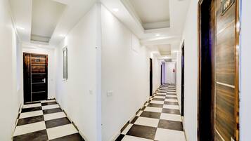 A hotel corridor with checkered flooring, white walls, and doors with room numbers.
