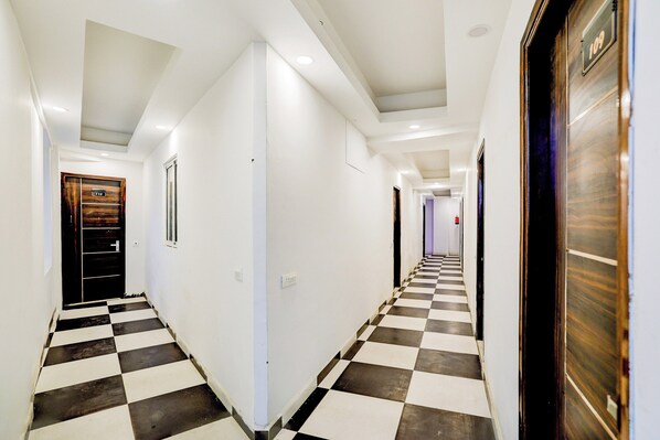 A hotel corridor with checkered flooring, white walls, and doors with room numbers.