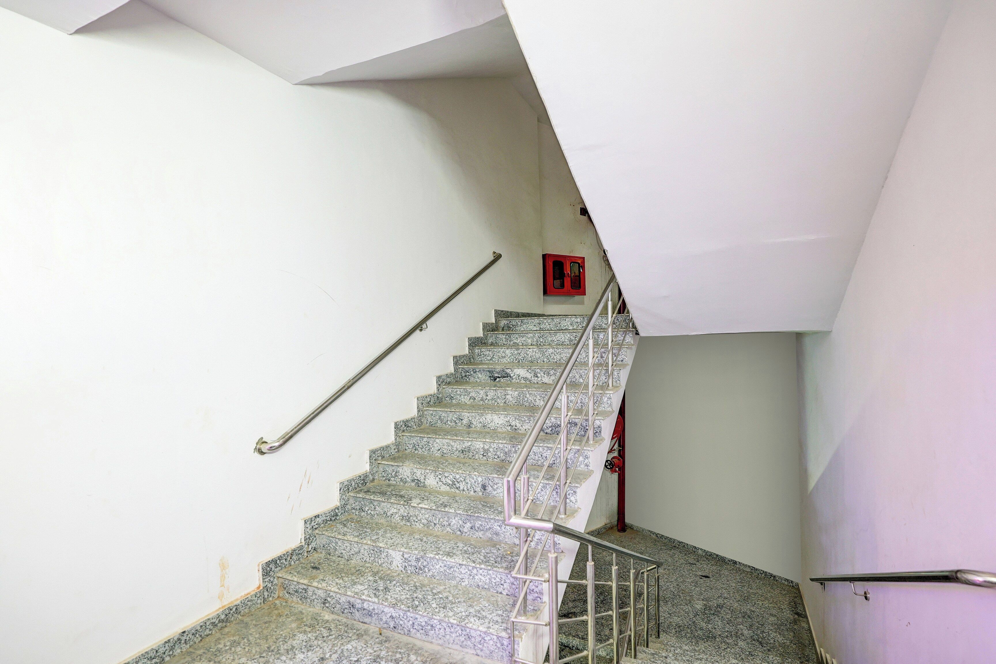 A staircase with a metal handrail and a red emergency exit sign on the wall.