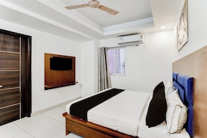 Un dormitorio con cama, ventilador de techo, equipo de aire acondicionado y ventana con cortinas.