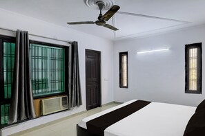 Une chambre d’hôtel avec un lit, un ventilateur de plafond, une fenêtre avec des barreaux et une porte.