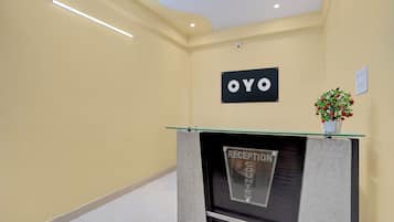 Un espace d'accueil avec un comptoir de réception, une enseigne indiquant « OYO » et une plante en pot accrochée au mur.