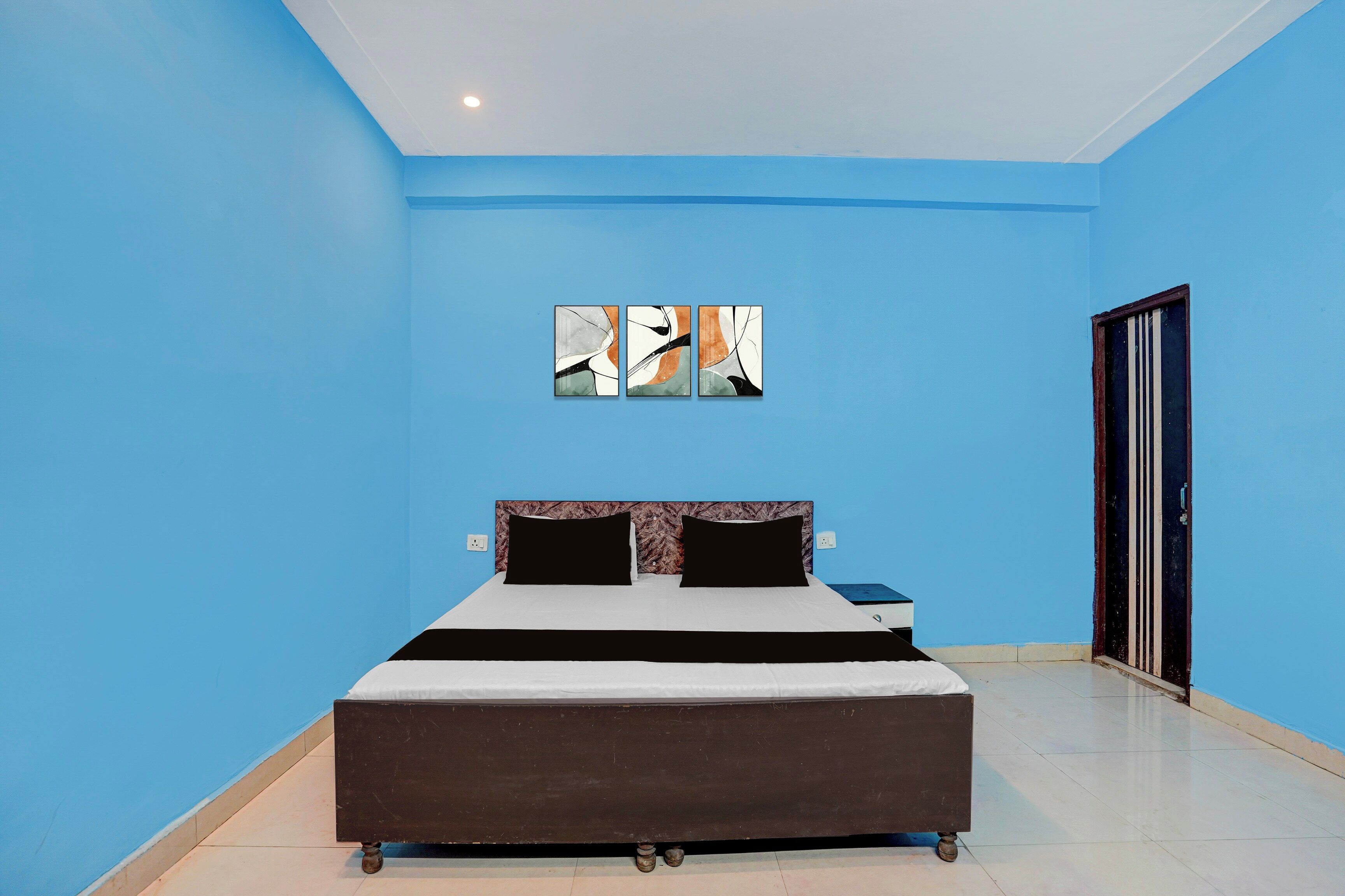 Une chambre à coucher comprenant un lit, une table de chevet, une œuvre d’art accrochée au mur et une porte.