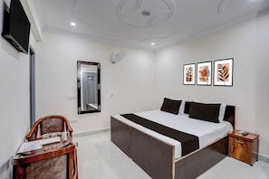 Ein Hotelzimmer mit einem Bett, einem Schreibtisch, einem Stuhl, einem Spiegel, einem Nachttisch und drei gerahmten Bildern an der Wand.