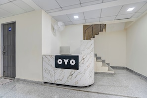 Ein Empfangsschalter mit einem Schild, auf dem 'OYO' steht, in einer modernen Lobby mit einer Treppe und einer Tür mit der Bezeichnung '002'.