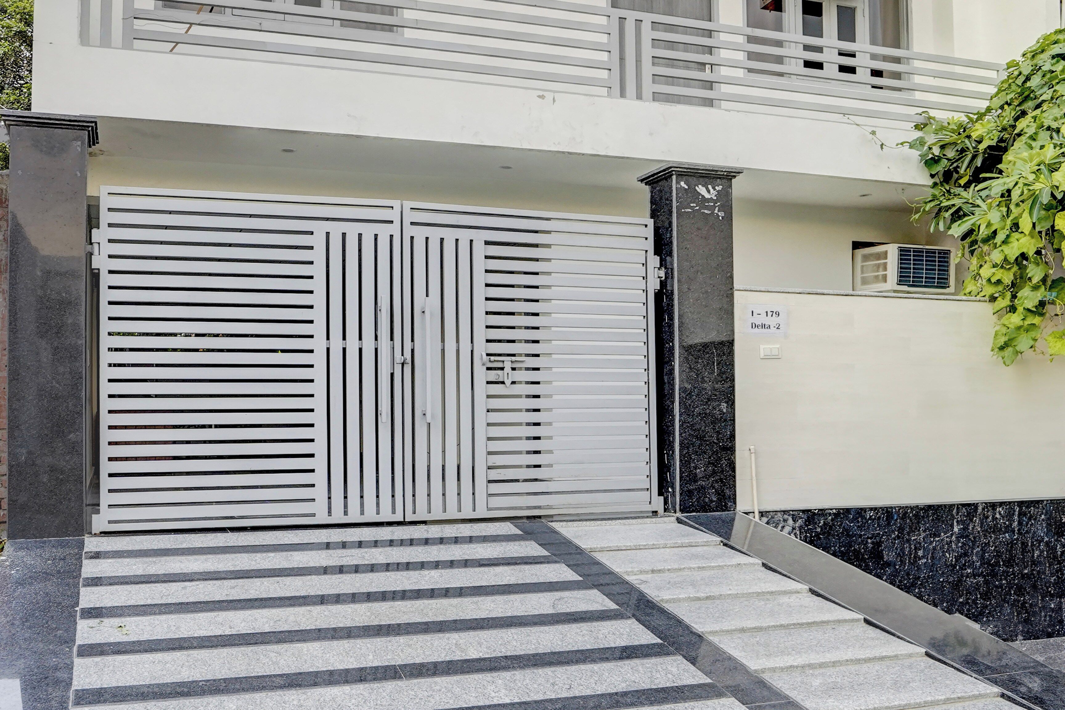 A gated entrance with a metal gate, a staircase leading up to a balcony, and a sign indicating the unit number.