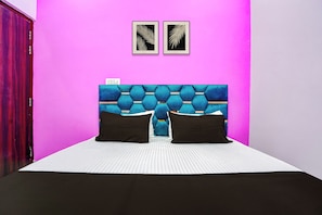 Un dormitorio con una pared rosa intenso, un cabecero azul capitonado, dos almohadas negras y una colcha a rayas.