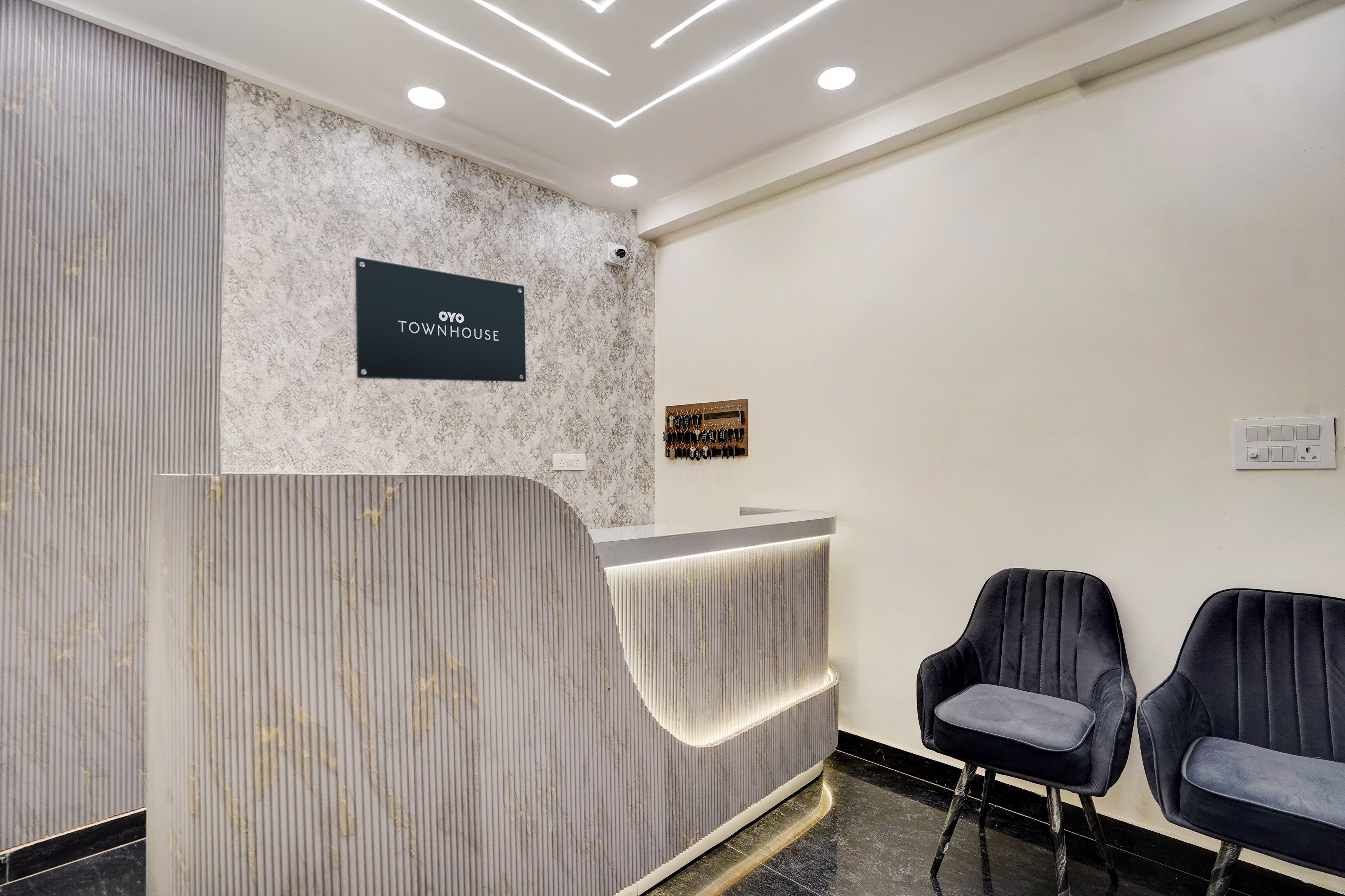 Un espace d’accueil avec un mur en marbre, une enseigne noire portant l’inscription « TOWNHOUSE », une caméra de surveillance et deux fauteuils rembourrés.