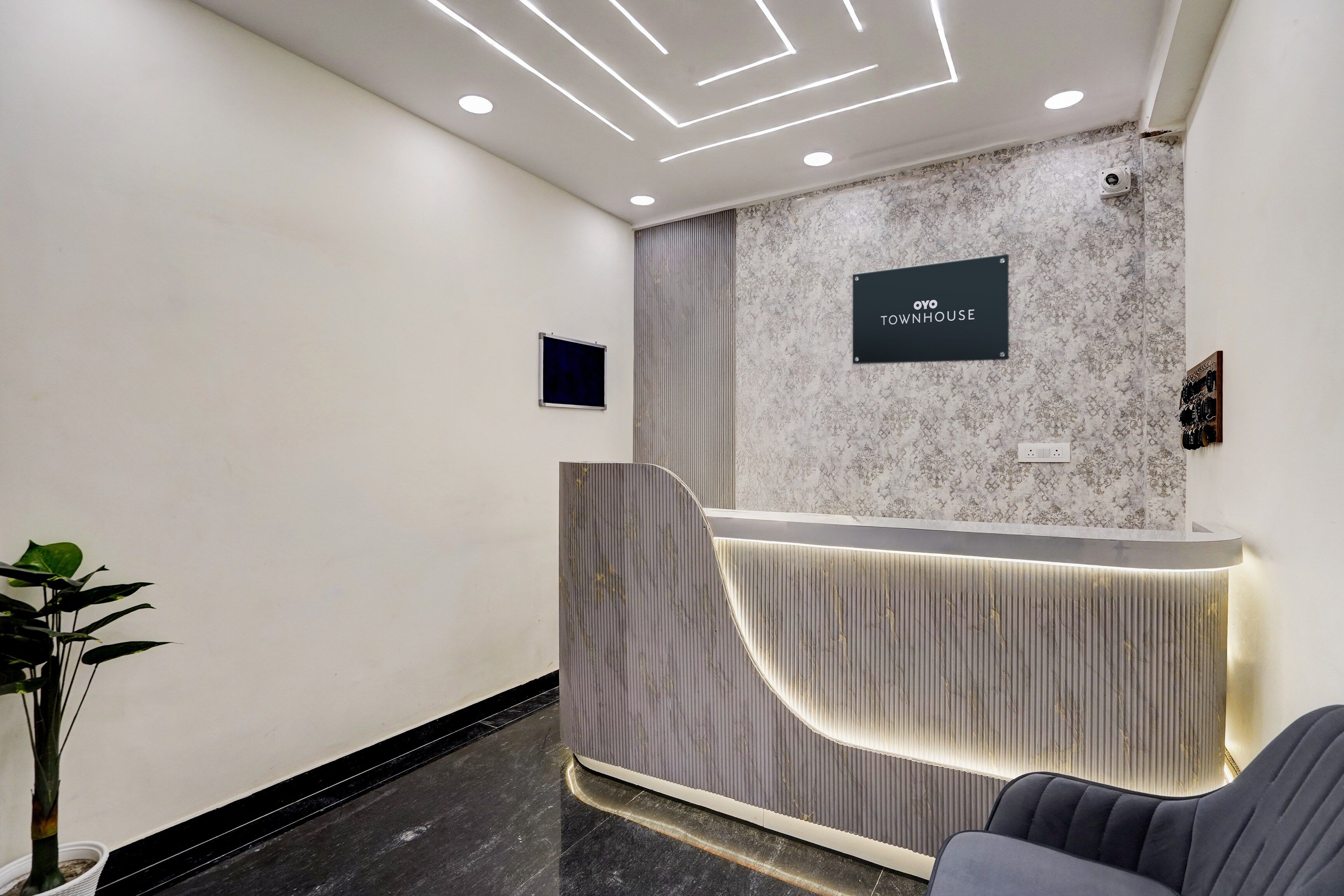 A reception desk with a marble-patterned wall, a sign reading 'OYO TOWNHOUSE', and a modern, illuminated reception area.