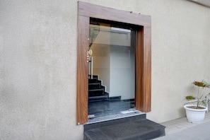 Uma porta de madeira com painel de vidro, um degrau que leva a uma escadaria e um vaso de planta ao lado da porta.