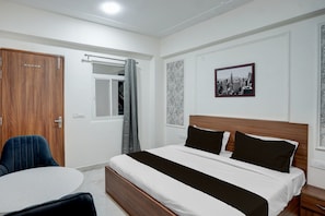 A hotel room with a bed, a desk, a chair, a window with a curtain, and a cityscape picture on the wall. - Townhouse Rosens hotel (Noida)