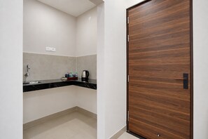 A small, modern bathroom with a wooden door, a sink with a faucet, and a countertop with a kettle and bottles. - Hotel O VINTAGE VAULTS (Noida)