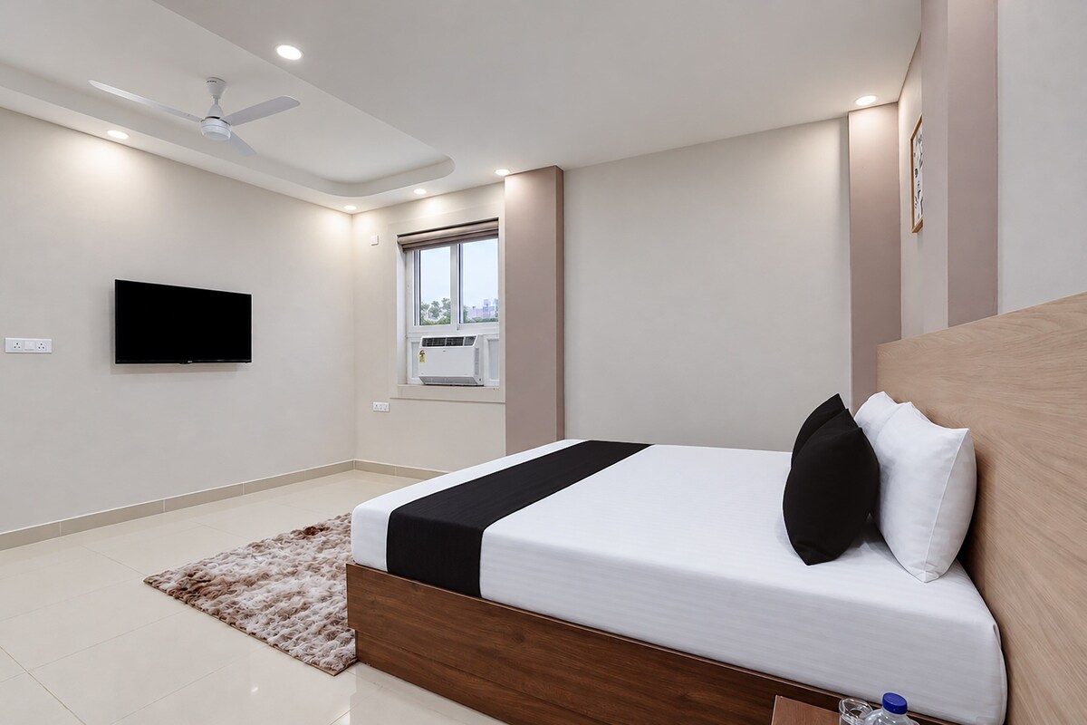 A modern bedroom with a bed, a flat-screen TV, a ceiling fan, and a window.