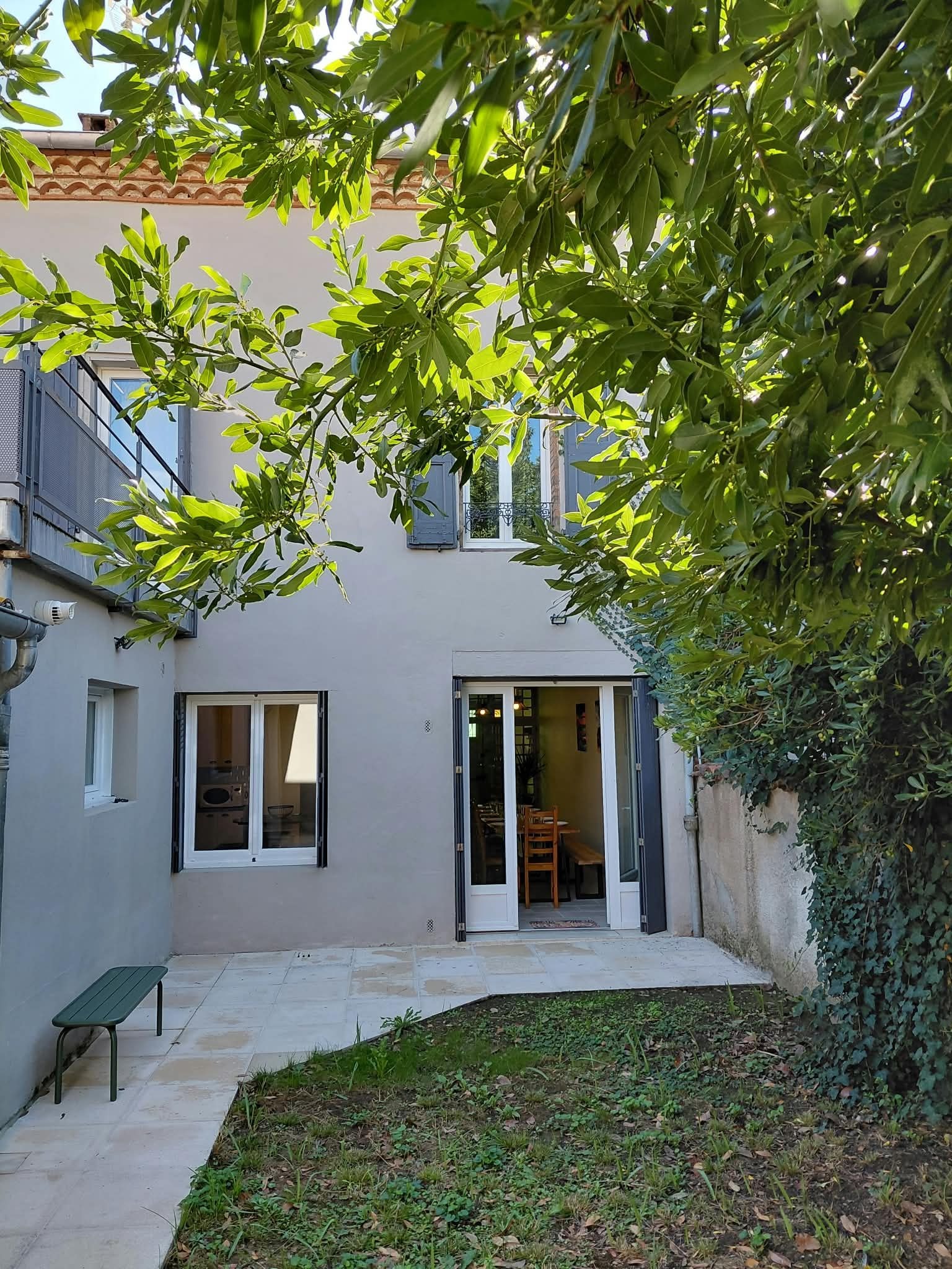 A residential building with a covered patio, a dining area with a table and chairs, and a small garden area.