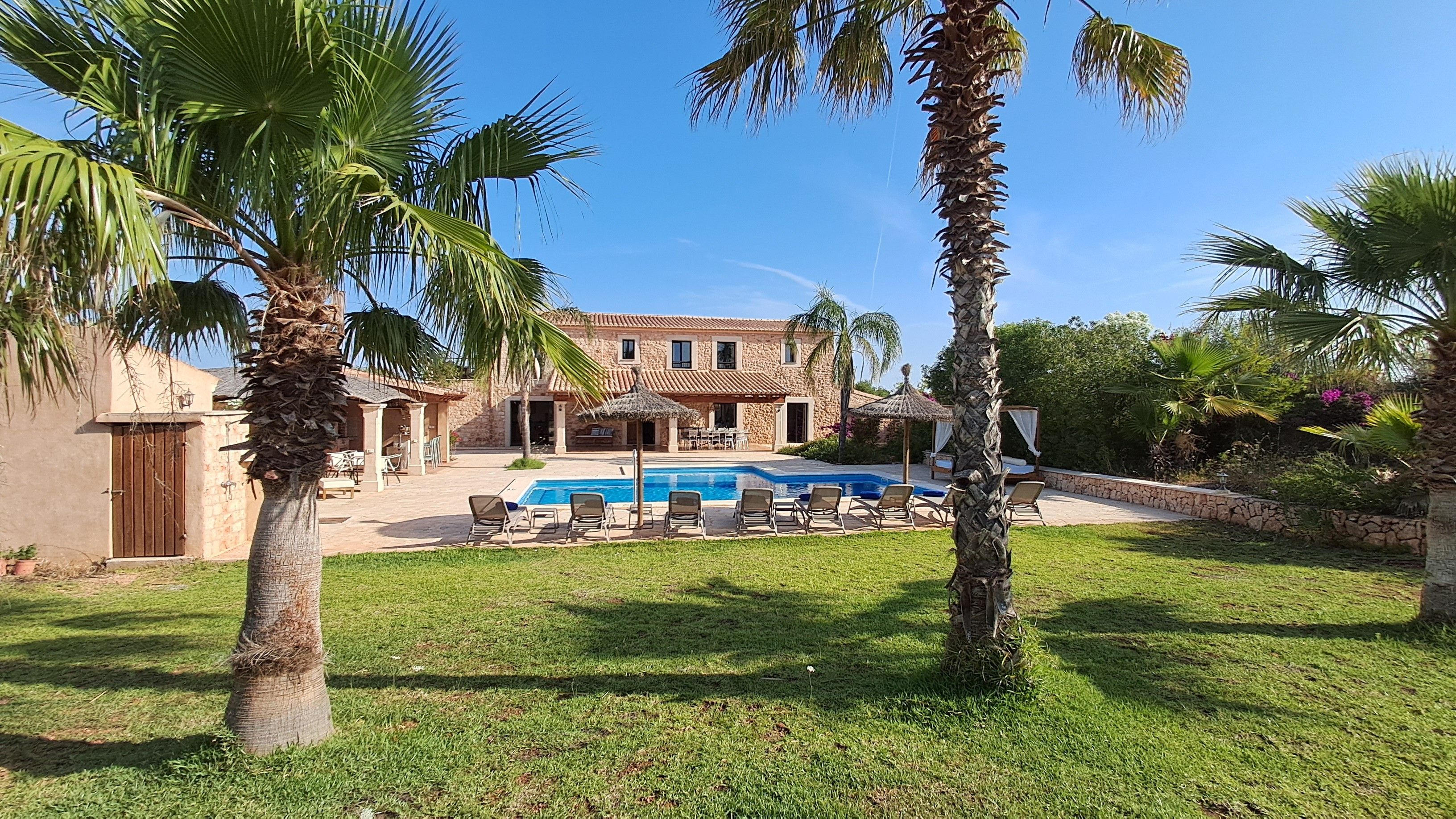 Eine Villa mit Swimmingpool, Sitzgelegenheiten im Freien und Palmen.