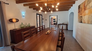 Een eetgedeelte met een houten tafel, stoelen, een kroonluchter en uitzicht op de keuken.