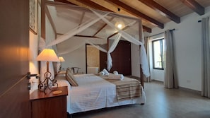 Een hemelbed met houten hoofdeinde, nachtlampjes en netjes opgevouwen handdoeken.