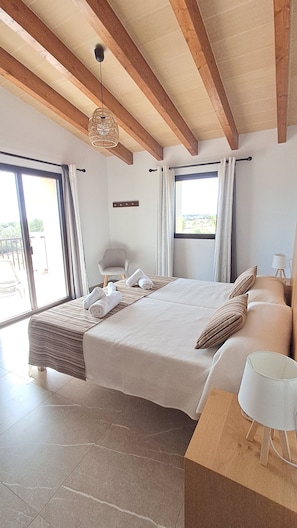 Un dormitorio con una cama grande, techo de madera, una ventana y una mesita de noche con lámpara.