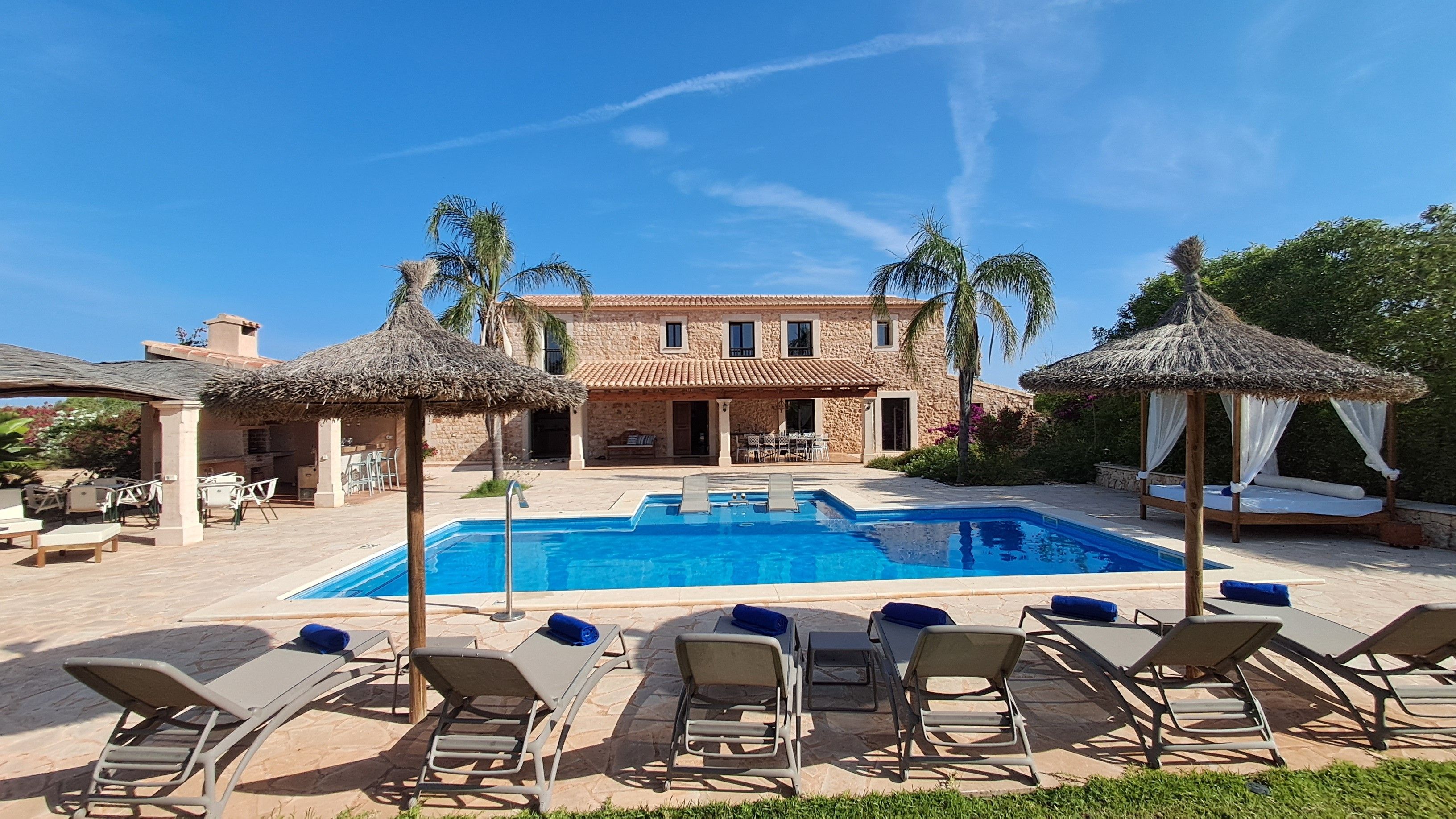 Un área de piscina con sillones de descanso y un edificio de piedra con tejado de baldosas.