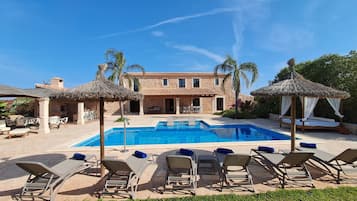 Un área de piscina con sillones de descanso y un edificio de piedra con tejado de baldosas.