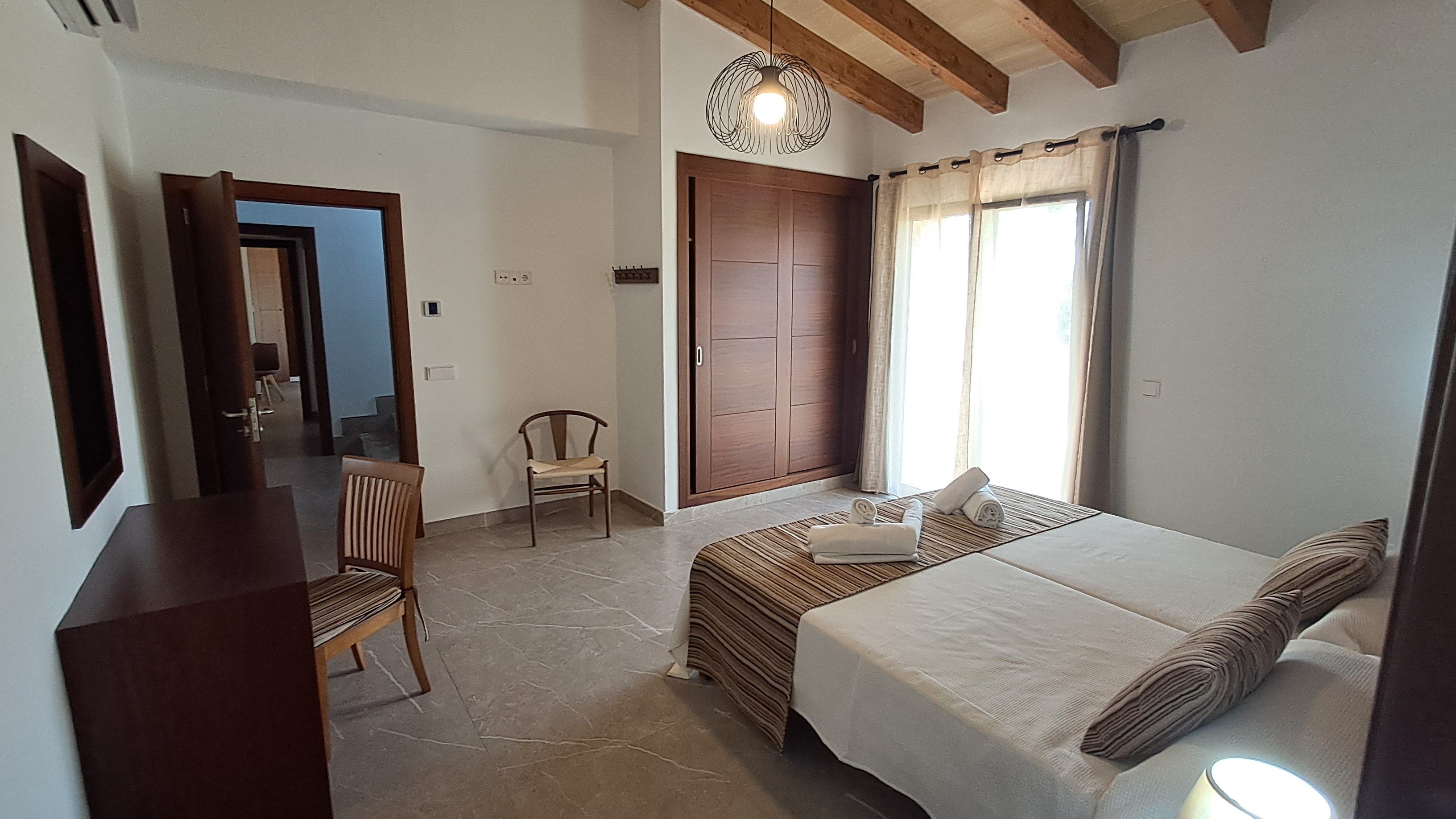 Un dormitorio con cama, una silla, un armario y una ventana con cortinas.