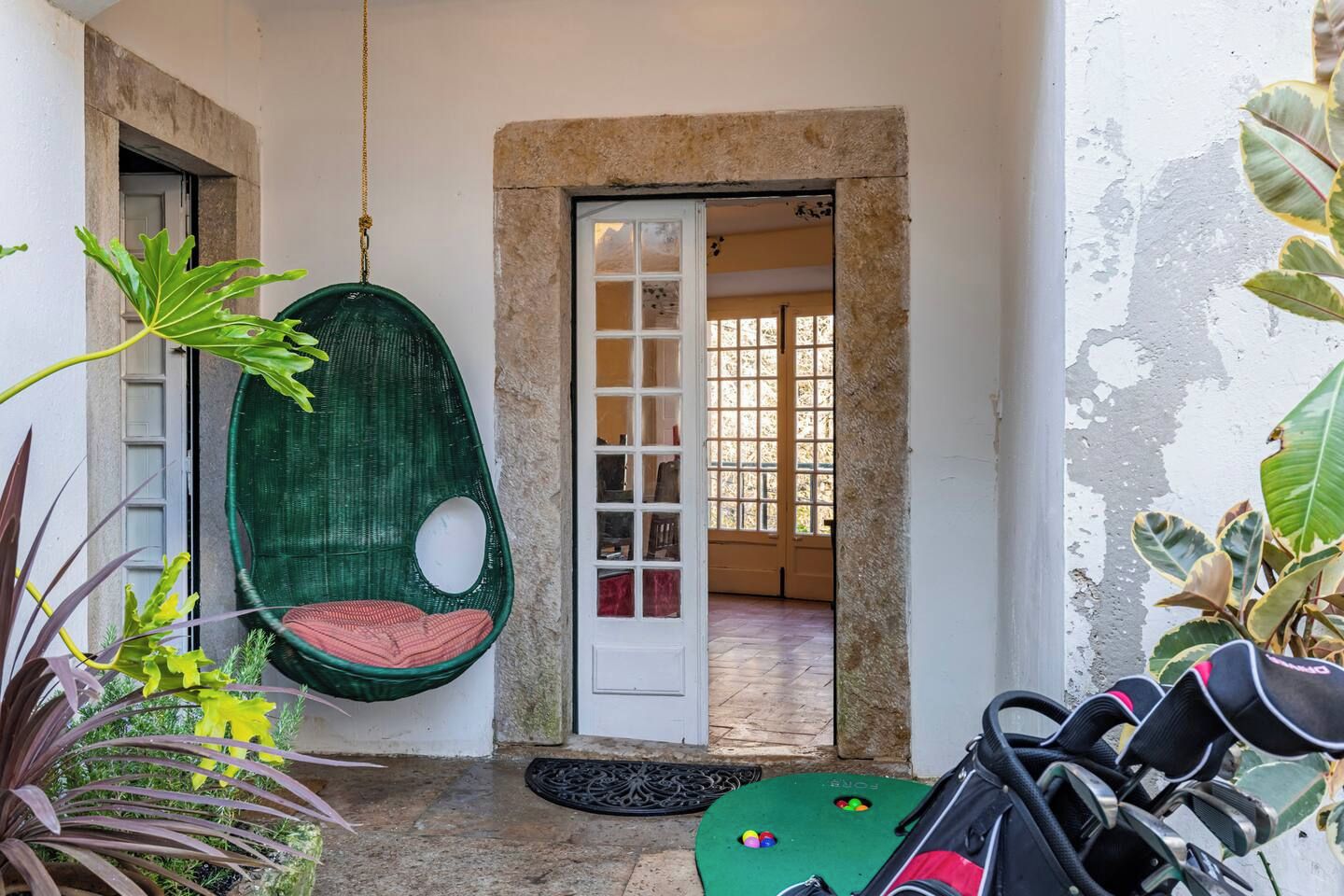 Une pièce avec un fauteuil suspendu, une porte donnant sur une autre pièce et une petite table avec des balles colorées.