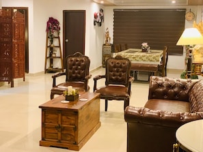 Una sala de estar con una mesa de centro de madera, sillones de cuero, un sofá, una mesa de comedor con mantel floral y un reloj en la pared.