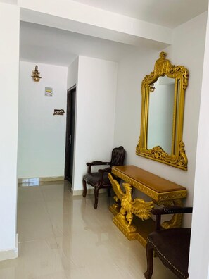 A hallway with a golden ornate mirror, a wooden console table, and a leather armchair. - Windsor House - Vintage Cottages (Shimla)