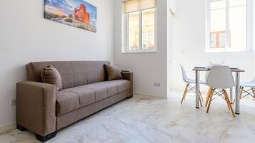 Una sala de estar moderna con un sofá, una mesa de comedor con sillas y un ventanal grande.
