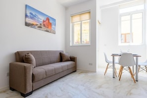 A modern living room with a sofa, a dining table with chairs, and a large window. - RODOLFU F5A (Tas-Sliema)