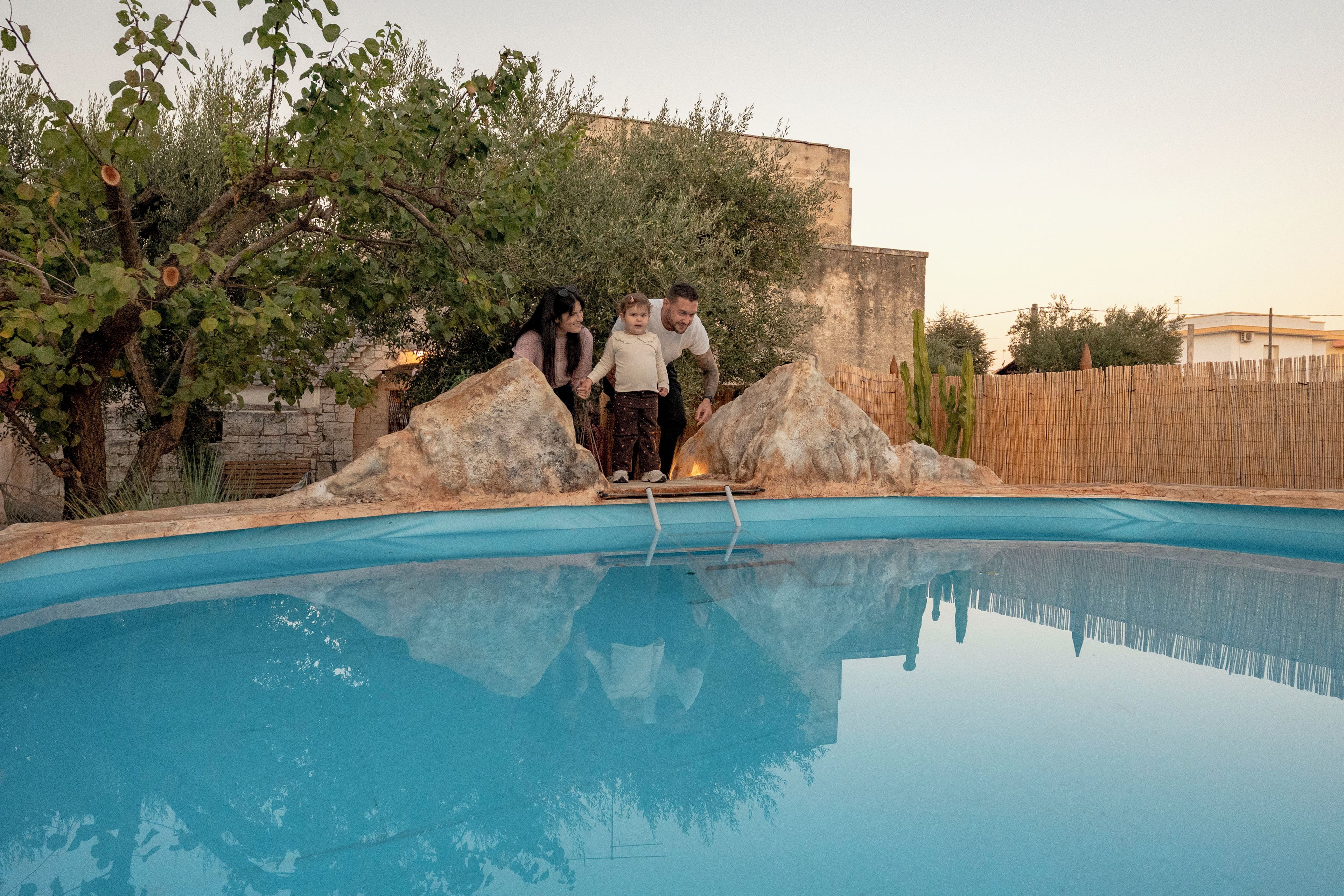 Une piscine avec un mur en pierre et une clôture en bois en arrière-plan.