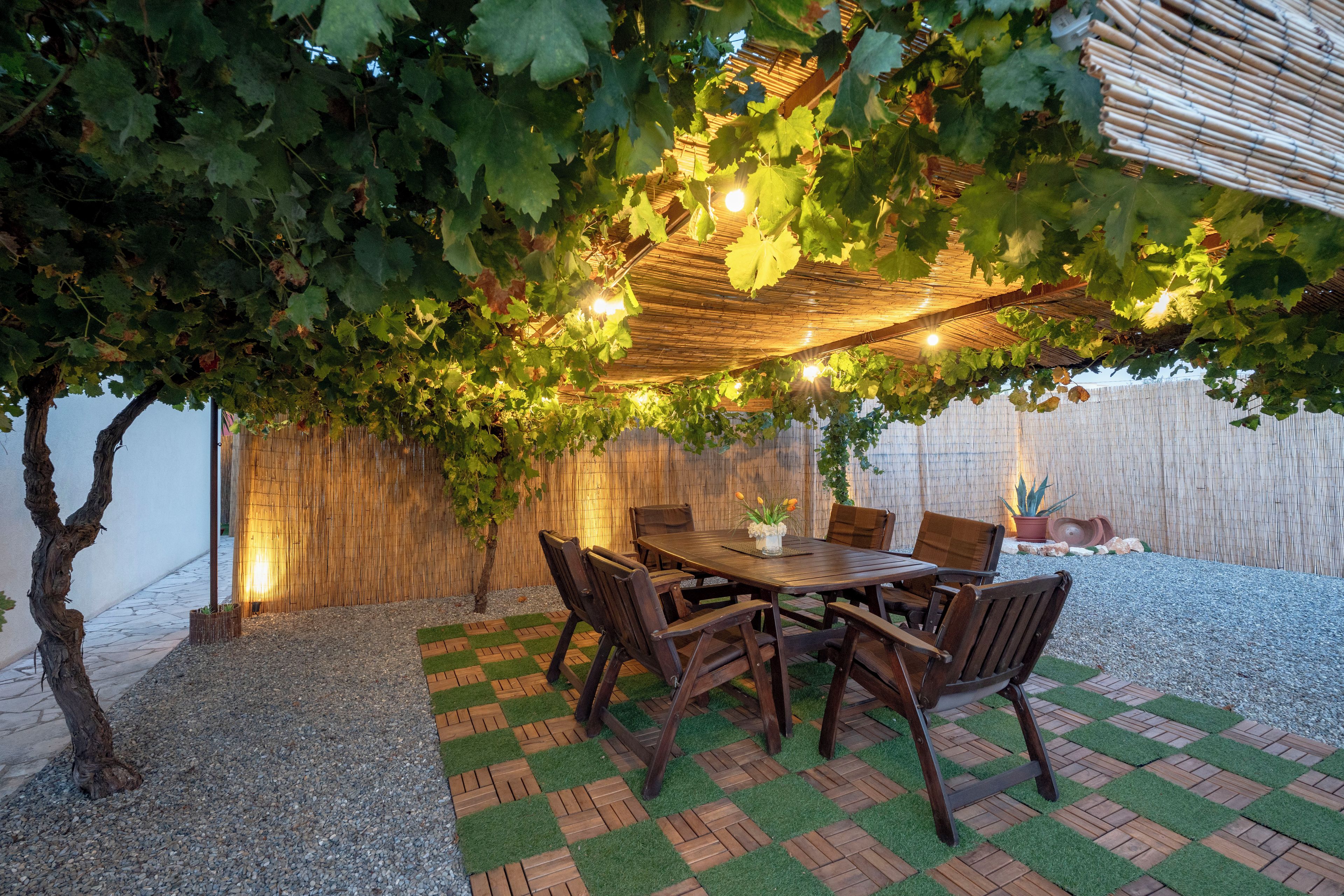 Un espace de restauration en plein air doté d’une pergola recouverte de vignes, d’une table en bois et de chaises.