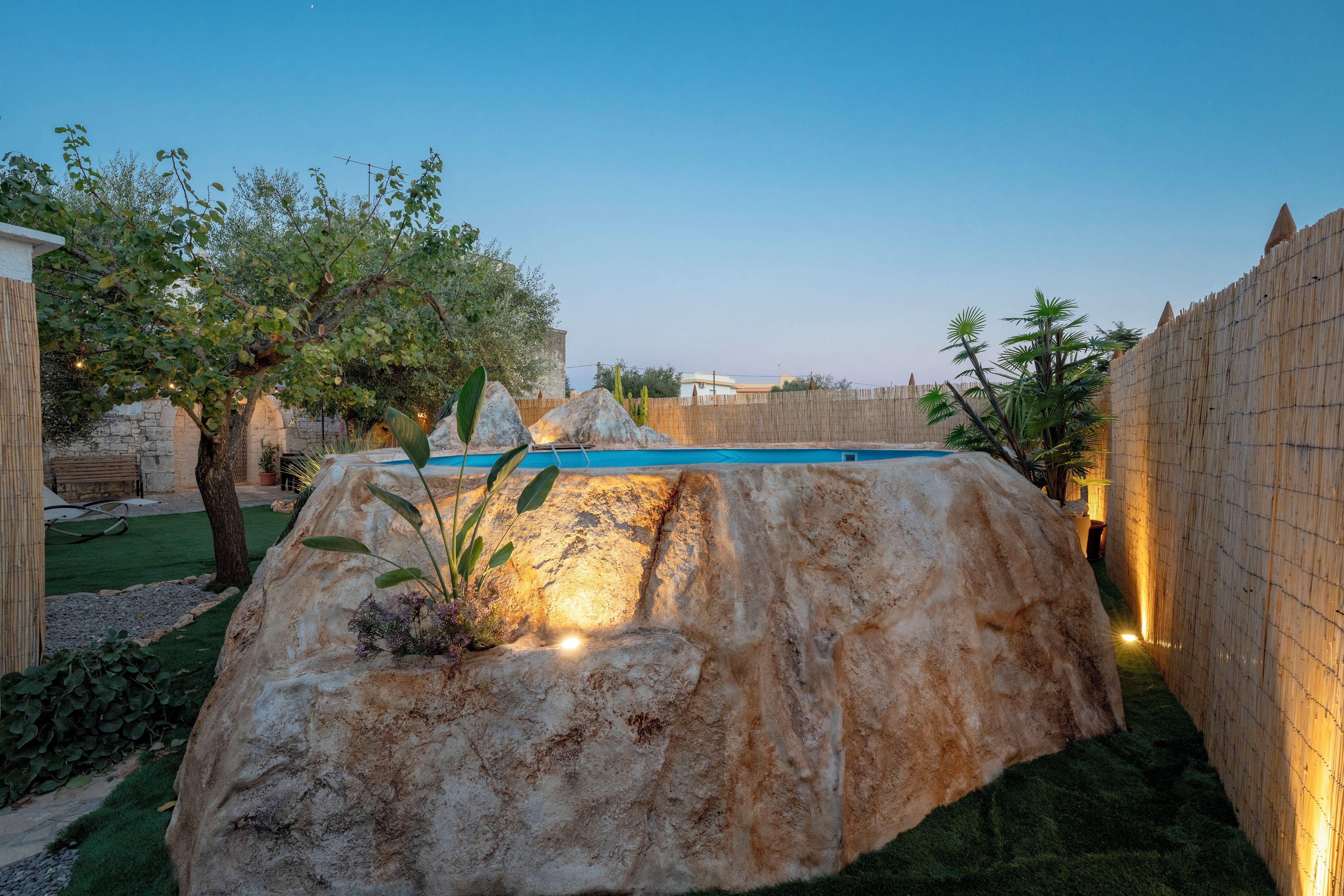 Un espace aménagé comprenant une piscine, un grand rocher décoratif et une clôture en bois.