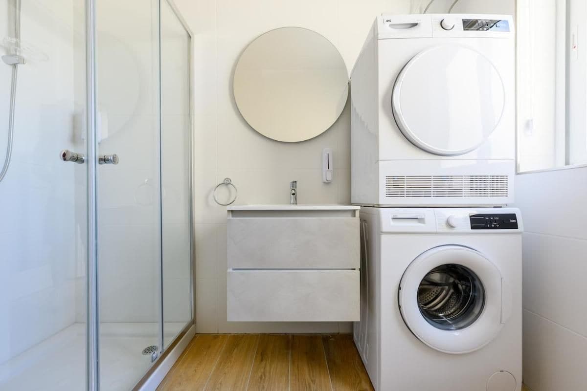 Un bagno compatto con box doccia in vetro, lavatrice e un piccolo lavabo con specchio.