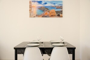 A dining table set for two with a painting of a coastal landscape above it. - RODOLFU F5B (Tas-Sliema)